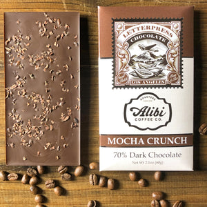 Mocha Crunch 70% Dark Chocolate packaging next to chocolate with nibs sprinkled on the backon wood table