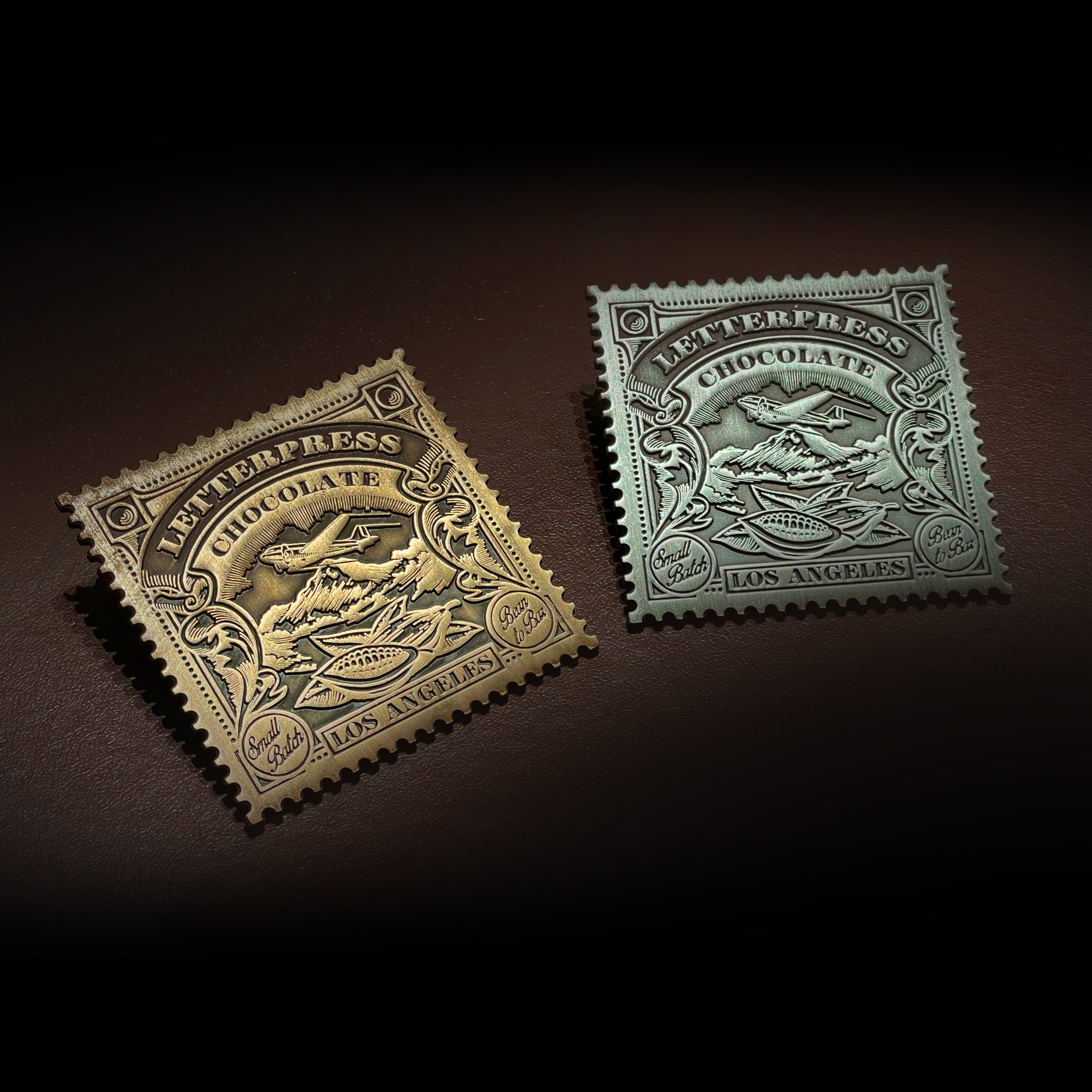 Gold and Silver pins with the company logo of a plane over a mountain inset in a 1920s vintage postage stamp design.